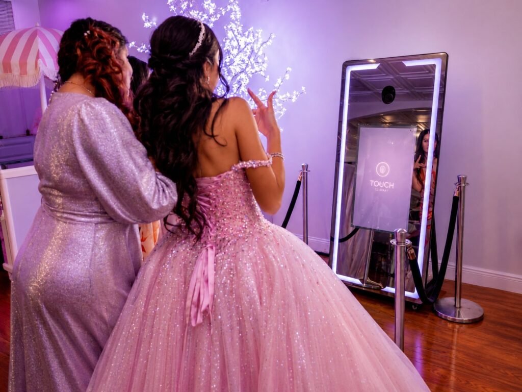Guests in formal attire using a mirror photo booth at a quinceañera celebration